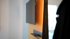 A modern room with a flat-screen TV mounted on a wall, a small shelf below it, and a door with a black frame.