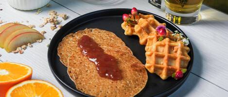 A plate with a pancake, waffles, and fruit on a table.
