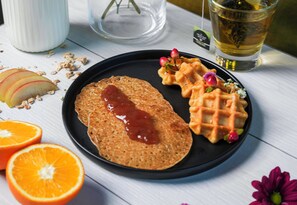 A plate with a pancake, waffles, and fruit on a table.