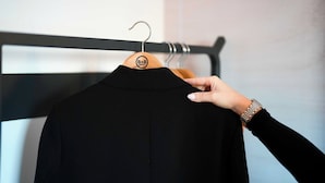 A black garment on a wooden hanger with a logo, held by a hand with a watch. - B&B Hotel Magnanville (Magnanville)