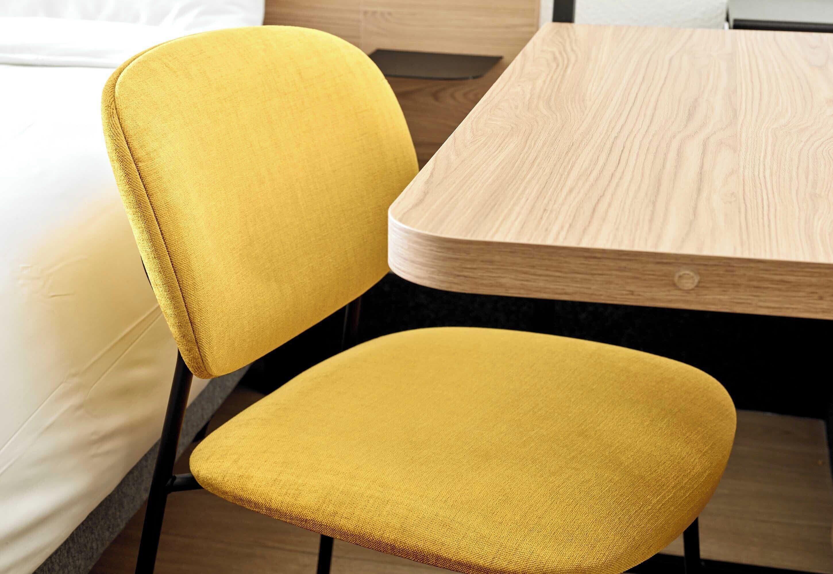 Una silla tapizada de color amarillo y una mesa de madera en una habitación con cama.