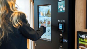 A person interacting with a touchscreen menu in a room with a wooden door and a wall-mounted sign. - B&B Hotel Magnanville (Magnanville)