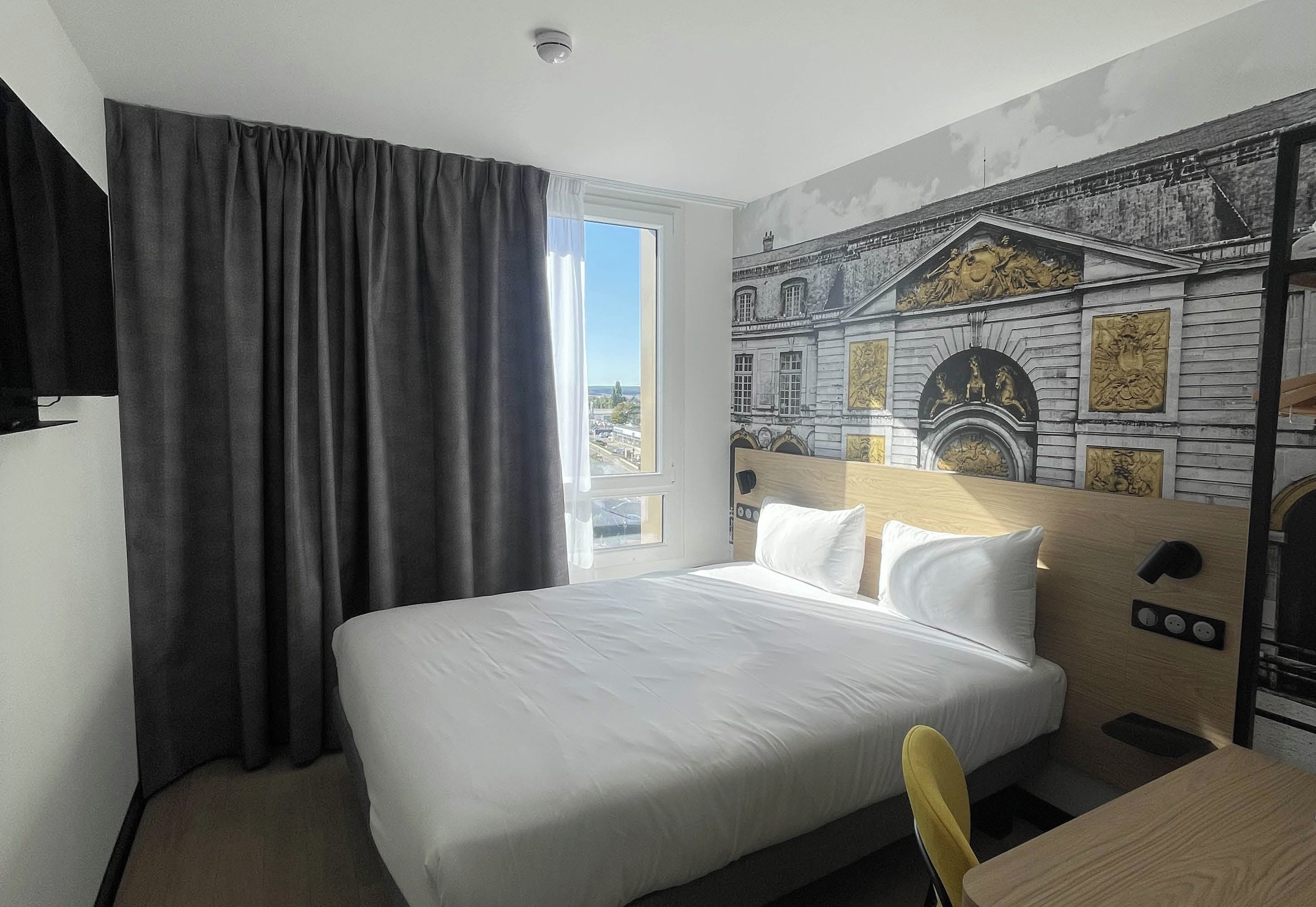 Een hotelkamer met een groot bed, een raam met gordijnen en een muurschildering.
