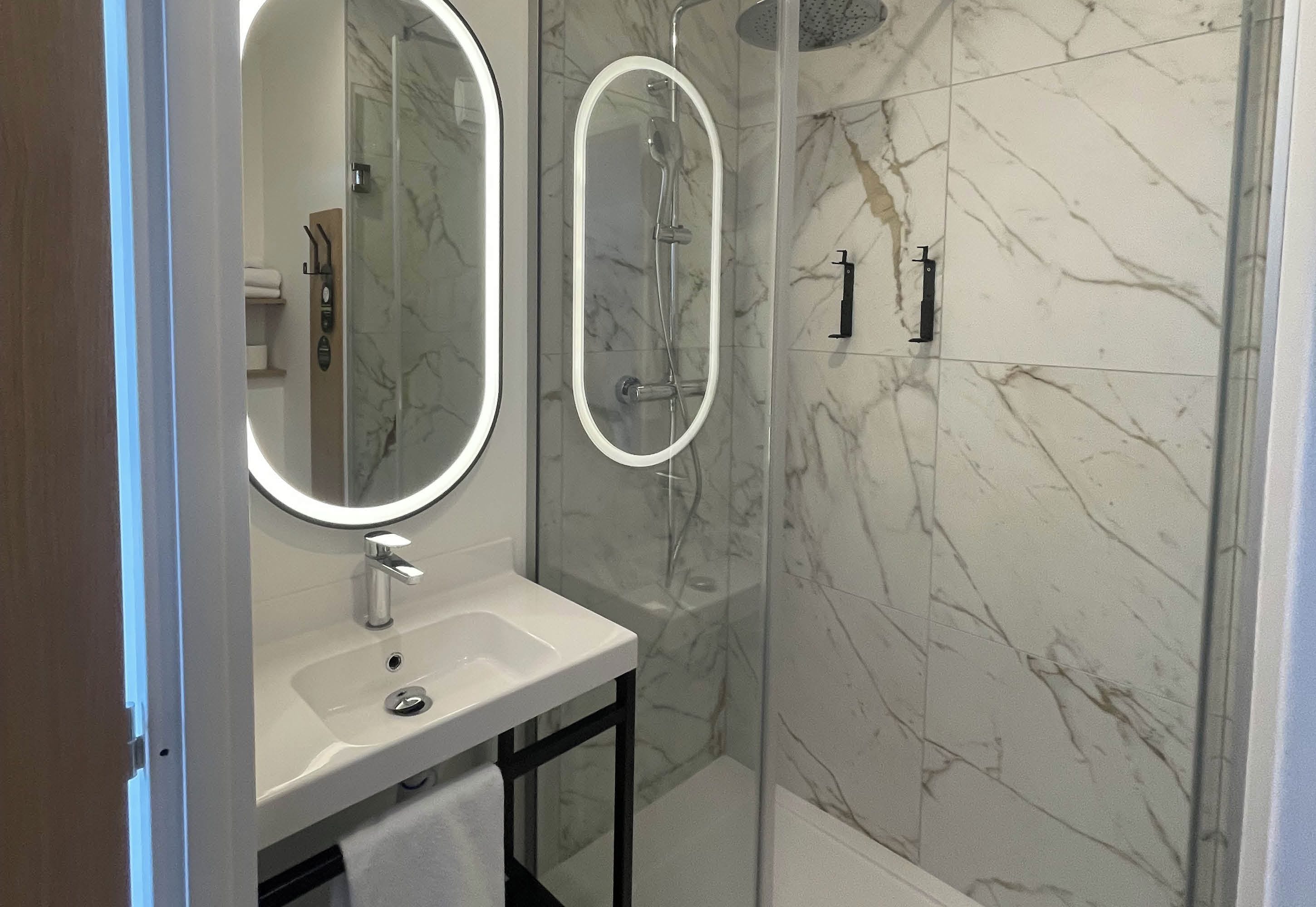 Une salle de bain avec une douche à parois de verre, un lavabo avec un miroir et des murs en marbre.