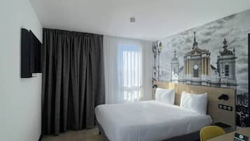Une chambre d’hôtel avec un lit, un téléviseur fixé au mur, une fenêtre avec des rideaux et une fresque représentant un bâtiment.