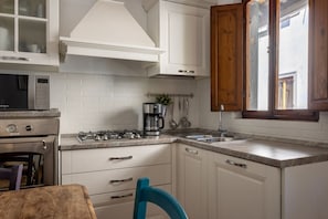 A kitchen with white cabinets, a stove, a sink, and a window with wooden shutters. - The Locksmith's house by Maison Florence (firenze)