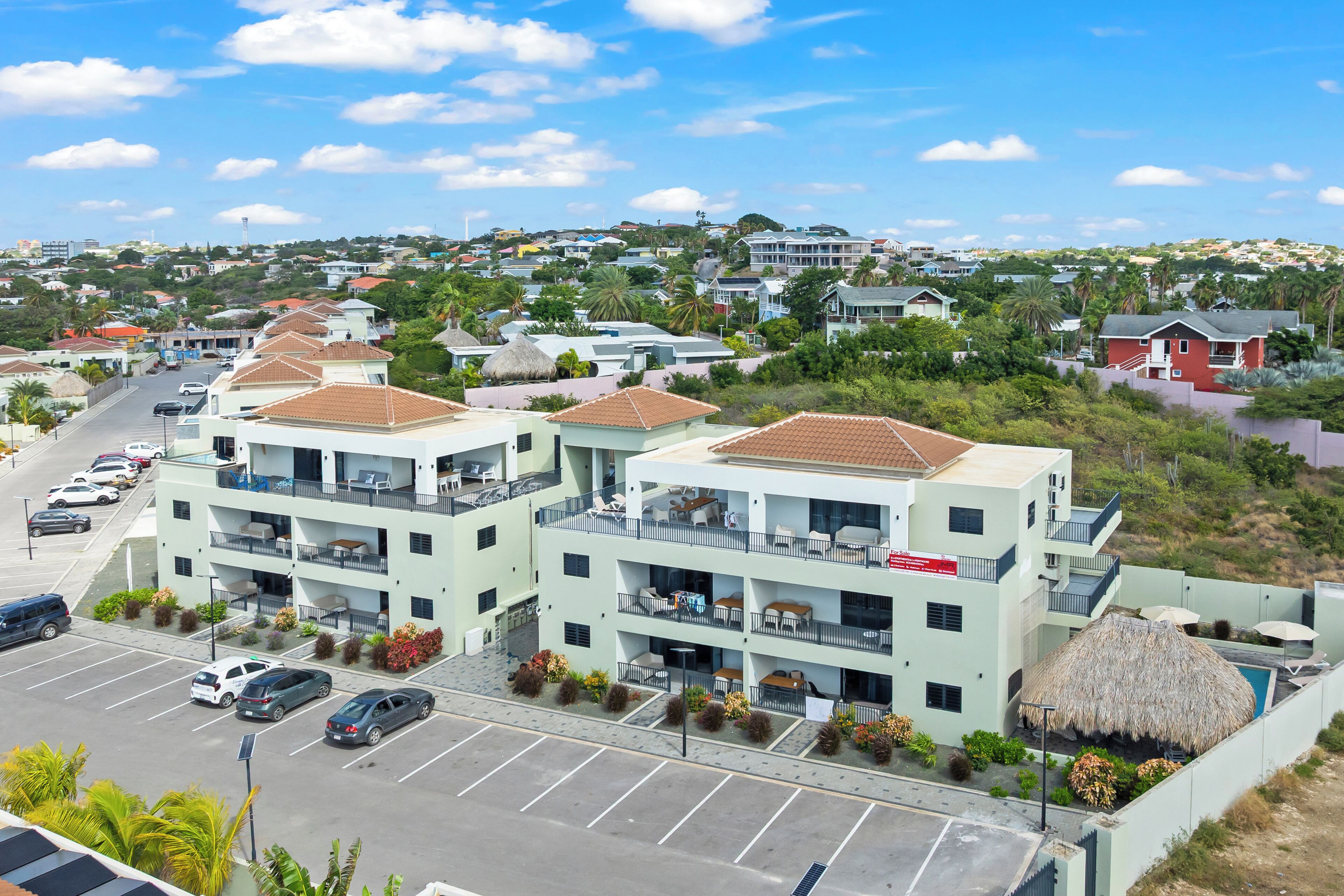 A multi-story hotel with balconies, a parking lot, and a view of a hilly town.