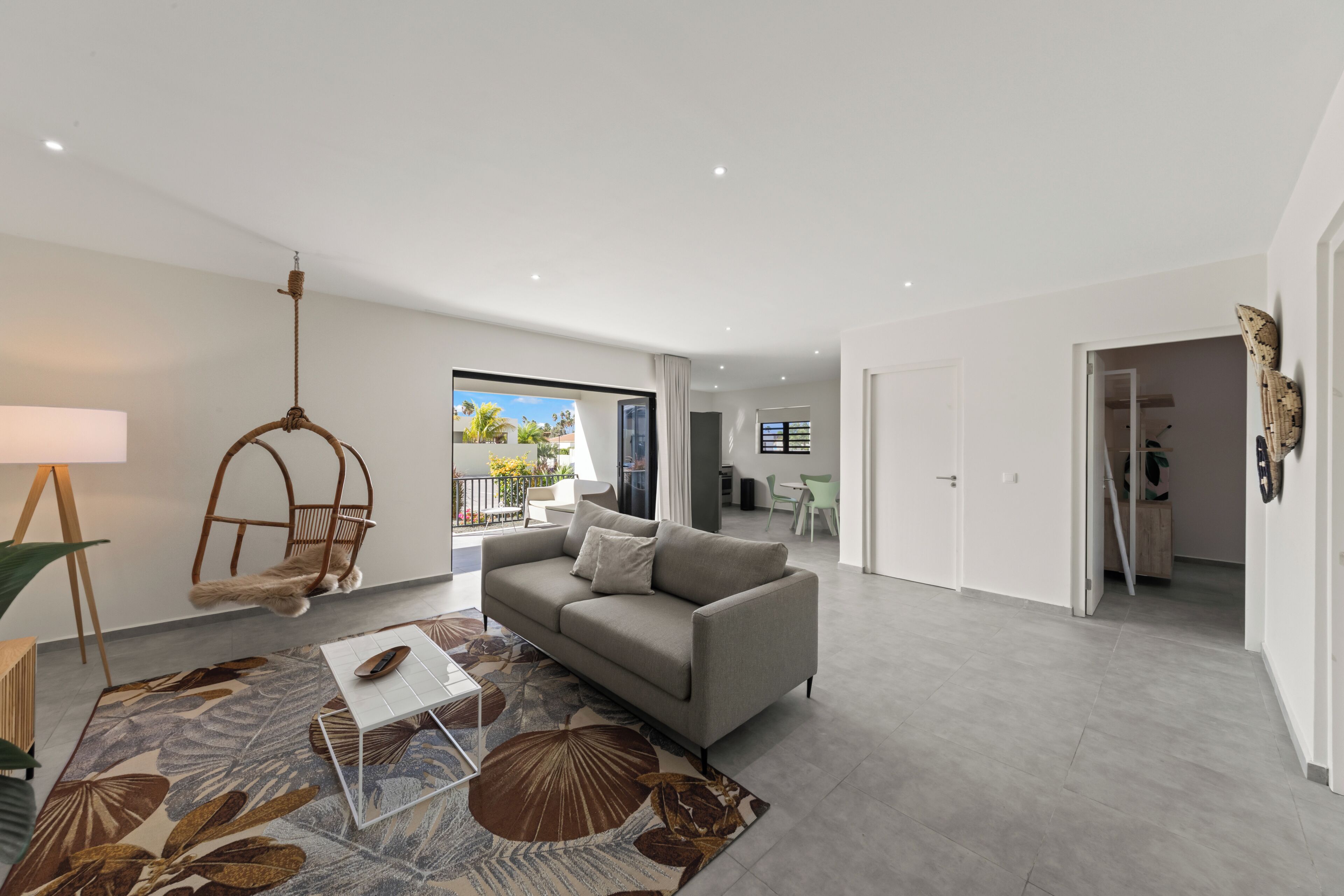 A modern living room with a grey sofa, a hanging chair, and a patterned rug.