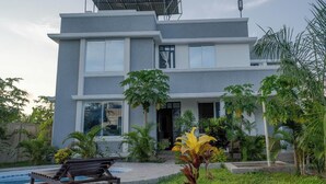 Uma casa moderna de dois andares com um painel solar, piscina e plantas tropicais.