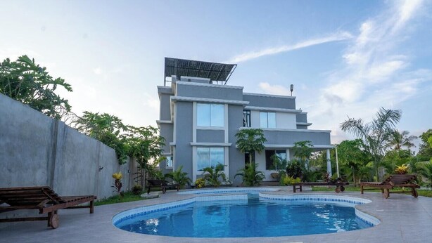 Uma casa moderna de dois andares com piscina, rodeada por vegetação e móveis de exterior.
