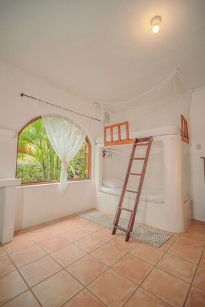 A room with a bunk bed, a ladder, a window with a view of greenery, and a tiled floor.