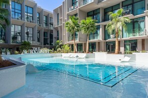 Ein modernes Hotel mit Schwimmbad, Palmen und blauem Himmel.