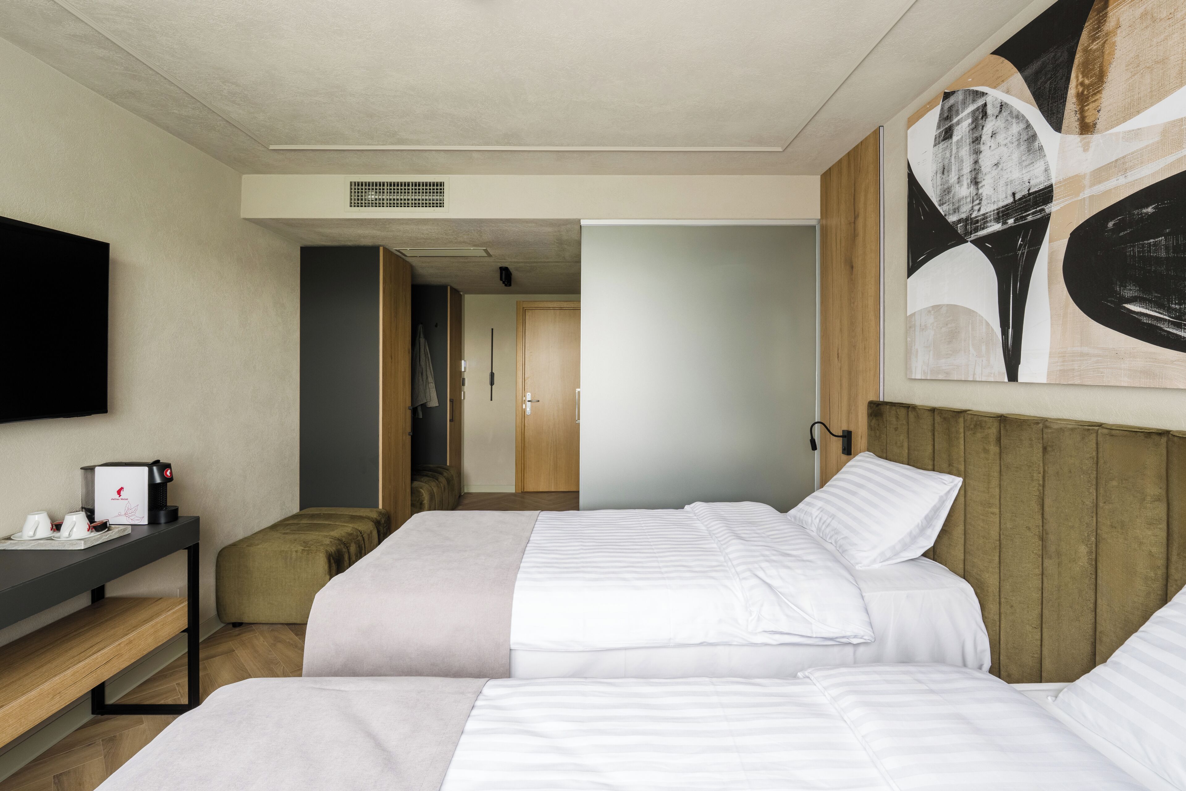 A hotel room with two beds, a desk, a flat-screen TV, and a painting on the wall.