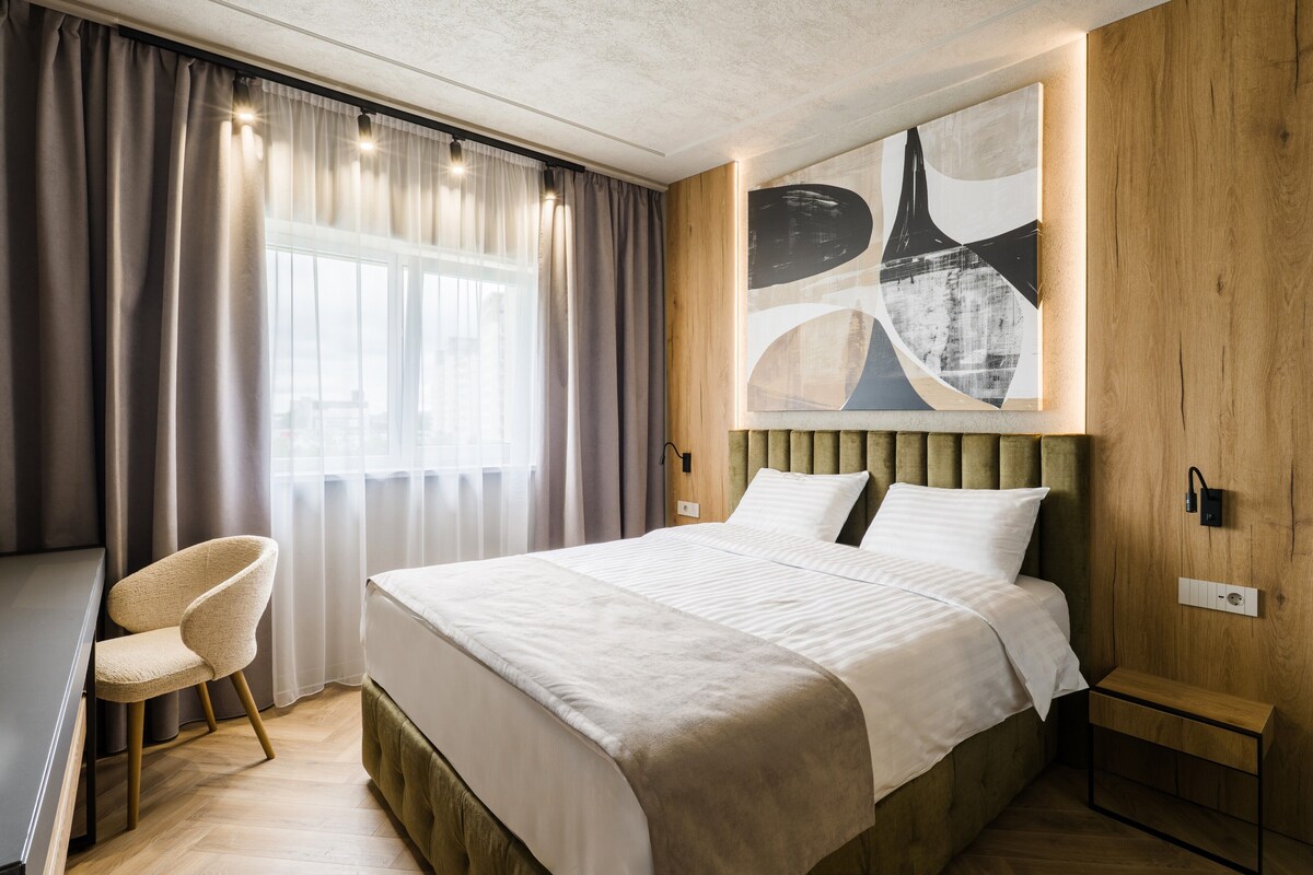 Un dormitorio moderno con cama, una silla, un cuadro y una mesita de noche.