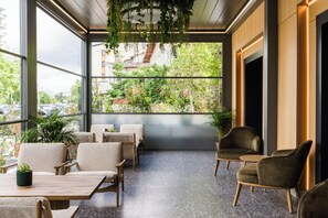 Un espacio interior moderno con asientos, mesas variadas y plantas colgantes, que ofrece vistas a la ciudad.
