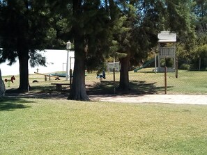 Ein Park mit Bäumen, einer Bank, einem Spielplatz und einem Wegweiser.