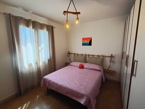 A bedroom with a bed, curtains, a hanging light fixture, a wall-mounted shelf, and a small painting. - Just a stone's throw from the sea—whether it's a sandy beach, rocky shore, or pebble beach—Casa Magia (Marina di Pisa-tirrenia-calambr)