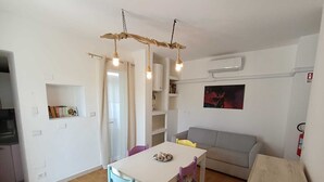 Un'area pranzo con tavolo e sedie, un divano grigio, una panca in legno e un lampadario.