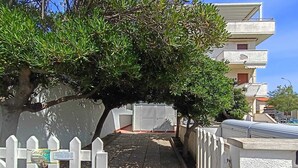 Un vicolo stretto con una recinzione in legno bianco, un albero e un edificio con facciata bianca e balconi.