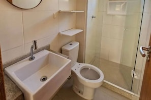 Kylpyhuone, jossa on pesuallas, wc ja lasinen suihkuseinä.