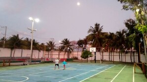 Een buitenbasketbalveld met een basketbalring, twee spelers en palmbomen op de achtergrond.