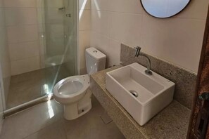 A bathroom with a toilet, a sink, and a glass shower enclosure. - Village Parque Stella Mares (Salvador)
