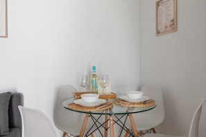 Et spisebord med glasplade, hvide stole, en flaske og vinglas på en vævet dug.