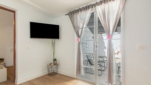 Un soggiorno moderno con una televisione a schermo piatto, una porta scorrevole in vetro con tende, un tavolino con una pianta e un pavimento in legno.