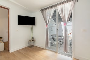 En moderne stue med et fladskærms-tv, en skydedør med gardiner, et lille sidebord med en plante og en trægulv.