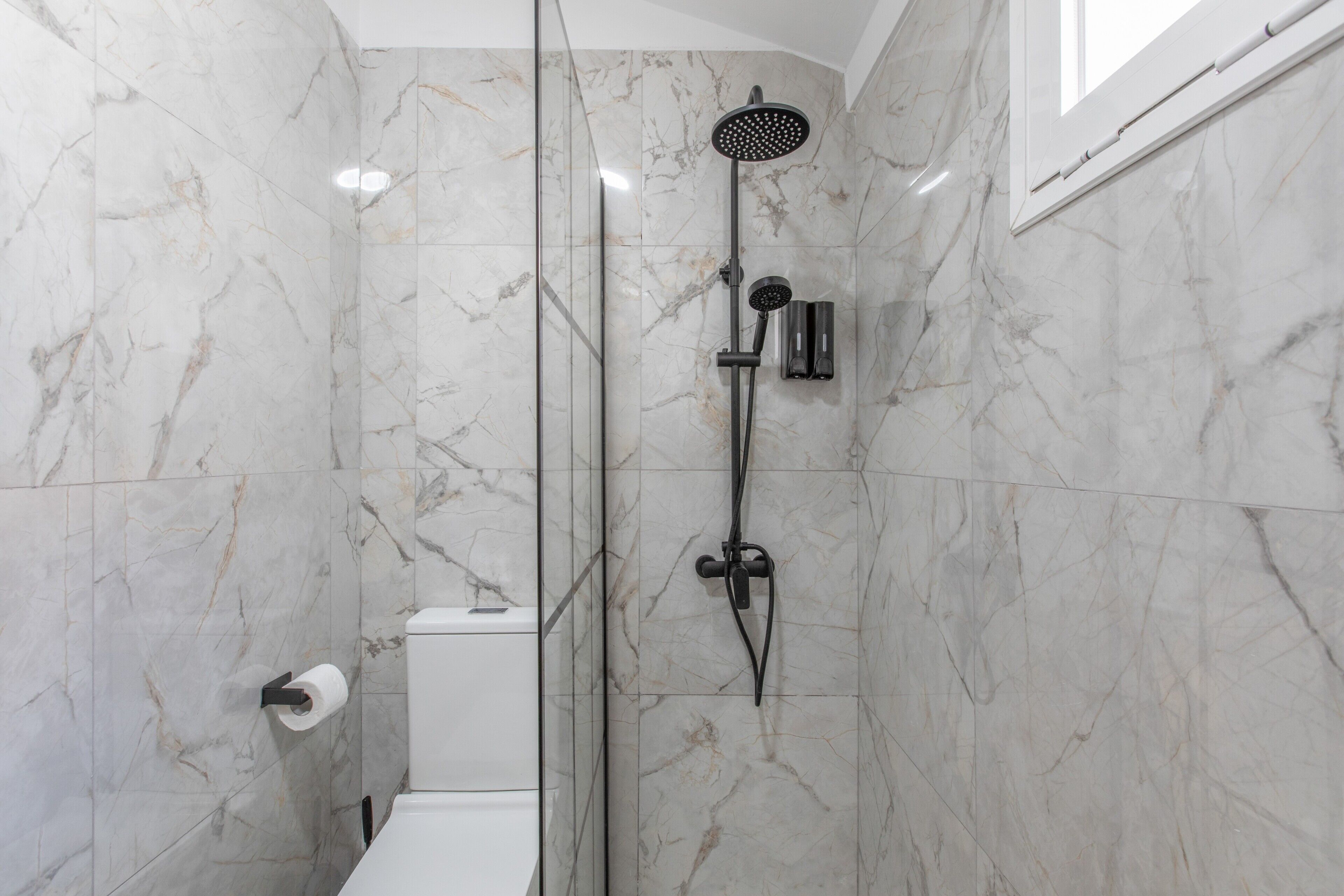 Een badkamer met een douche met glazen wand, marmeren wanden en een toilet.