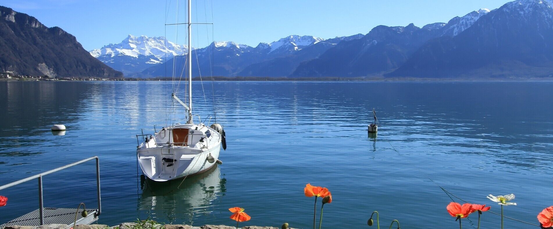 A sailboat docked at a pier with a mountainous backdrop.