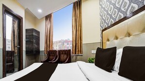 Habitación de hotel con una cama grande, una zona de estar con sillones, un ventanal con cortinas y una pared con diseño.