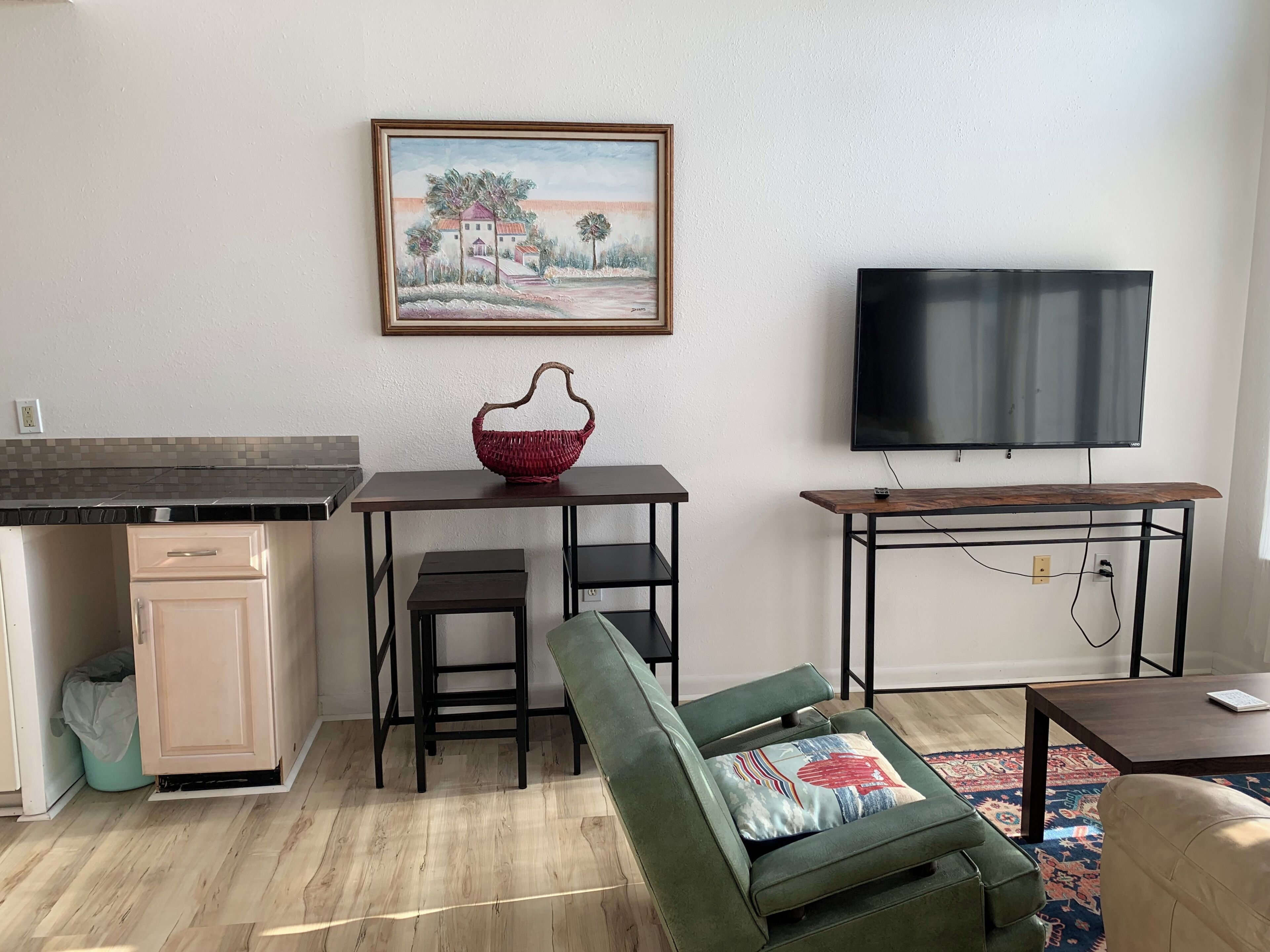 Un soggiorno con un divano verde, un tavolino con un cesto rosso, una TV su un mobile e un quadro appeso al muro.