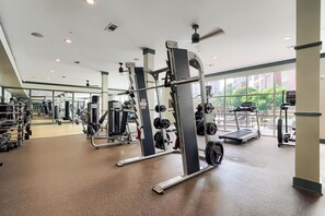 A gym with various exercise equipment, large windows, and a ceiling fan. - Heart of The Gulch | 1BR+Den | Sleeps 4 (Nashville)