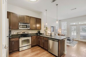 A modern kitchen with stainless steel appliances, wooden cabinets, and a large island. - Heart of The Gulch | 1BR+Den | Sleeps 4 (Nashville)