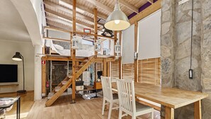 A spacious room with a wooden dining table, white chairs, a staircase, and a stone wall. - Vacation Home 'Atlantic Dream' with Sea View, Private Terrace and Wi-Fi (Costa Calma)