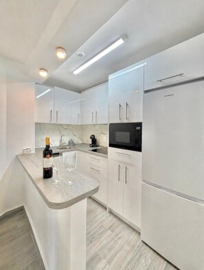 A modern kitchen with white cabinetry, a built-in microwave, and a wine bottle on the counter. - TERRASOL TRINIDAD APARTMENT (Torre del Mar)