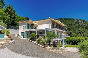 Ein zweigeschossiges Haus mit Balkon, einem Steinweg und Blick auf einen Berg.