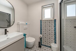 Une salle de bain avec un lavabo, des toilettes et une douche, le tout de couleur blanche.