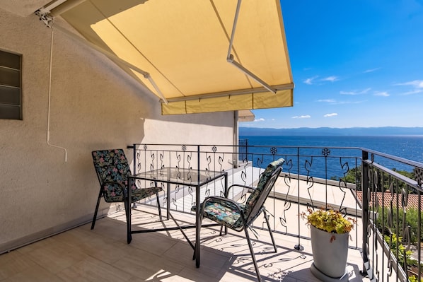 Een balkon met een tafel en stoelen, een bloempot en uitzicht op zee.