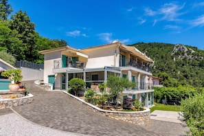 A two-story house with a balcony, surrounded by greenery and a mountain backdrop. - Beachside Villa Mia Apartments (Lovran)