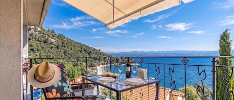 A balcony with a table set for two, overlooking a coastal view.