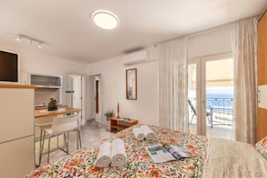 A hotel room with a bed, a desk, a chair, a TV, and a balcony with a view. - Beachside Villa Mia Apartments (Lovran)