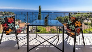 Varanda com mesa e cadeiras, vista para o mar e uma cordilheira distante.