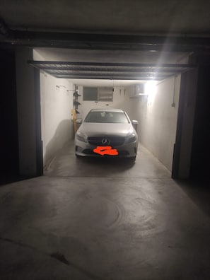 Ein Auto steht in einer schlecht beleuchteten Garage mit Betonböden und -wänden, und eine einzelne Lichtquelle hängt von der Decke.