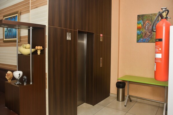 Una habitación de hotel con un armario de madera, una mesa verde, un extintor y un cubo de basura.