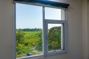 A window with a view of a green landscape and trees. - Hotel Flora (Haridwar)