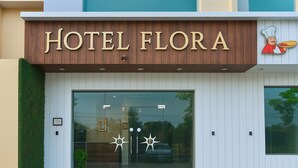 Hotellin sisäänkäynti, jossa on kyltti, jossa lukee ”HOTEL FLORA”, lasiovi ja pieni ruukussa oleva kasvi.