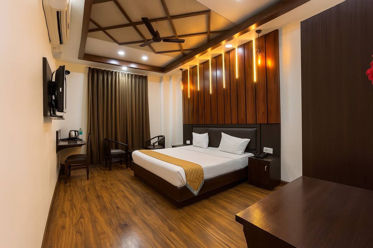 Habitación de hotel con cama, mesita de noche, silla, escritorio y televisor montado en la pared.