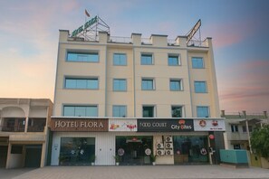 Ein mehrstöckiges Hotel mit einem Schild für 'Hotel Flora' und einem 'Food Court' mit dem Restaurant 'City Bites'.